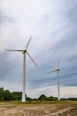 Fototapeta premium Low angle shot of two white wind turbines with spinning motion-blurred blades in an agricultural field under an overcast cloudy sky in Latvia.