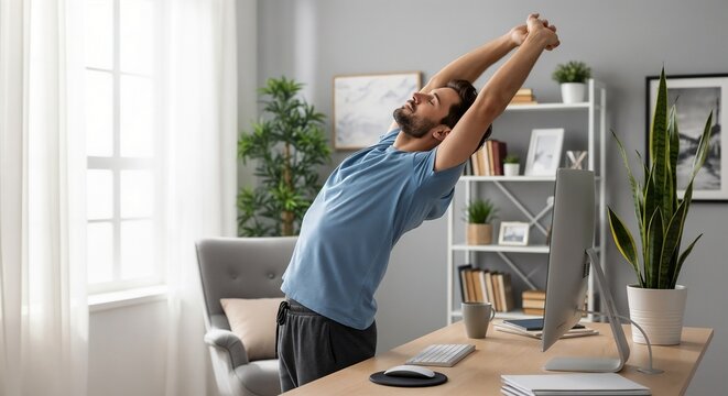 Man standing at desk taking stretching break to relieve tension in home office. Simple stretching break improves posture and vitality. Male worker enjoying stretching break for daily office wellness.