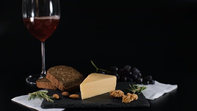 Hand pouring wine near composition of fresh cheese with walnuts, almonds, bread and rosemary. Grapes are behind on a black background. Gourmet food and tasting concept