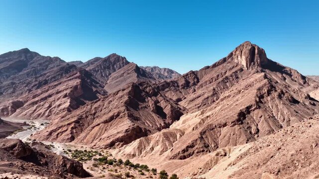 Rugged mountain peaks under a clear blue sky during a slow drone pan revealing vast arid landscapes