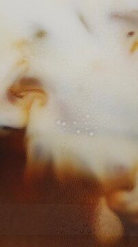 4K Vertical video Macro texture shot of white milk mixing with iced espresso coffee inside glass, swirl waves and liquid motion background for specialty coffee shop menu concept.