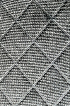 Primer plano de una textura textil de color gris oscuro con un patr&oacute;n geom&eacute;trico de rombos en relieve y detalles de tejido entrelazado.