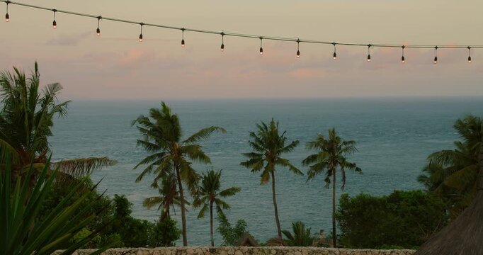 String lights hang over palm trees and deep blue sea during sunset in tropical Bali