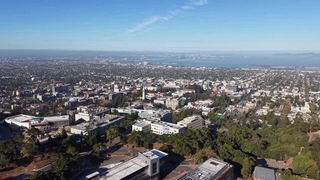 Expansive aerial view of the University of California, Berkeley campus, with the cityscape stretching towards the San Francisco Bay and Golden Gate Bridge on a clear, sunny day