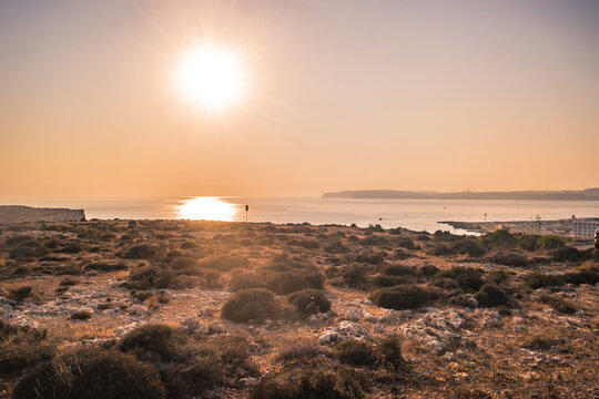 Hilltop panorama with arid landscape, sun shining above the sea and islands on the horizon, Cirkewwa MALTA
