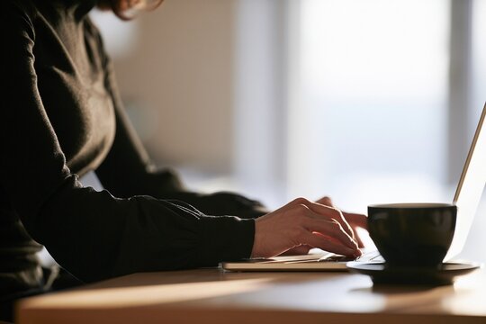 Woman typing on a laptop computer with a cup of coffee at a desk