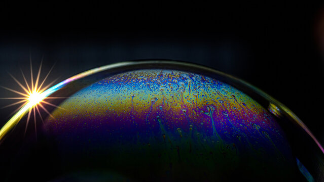 Iridescent soap bubble creating colorful fluid physics pattern