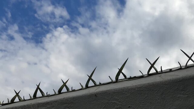 Cloudy sky above defensive sharp metal security spikes on wall top.