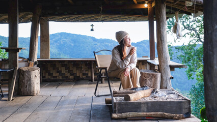 Naklejka premium A woman drinking coffee on wooden terrace and looking at nature views