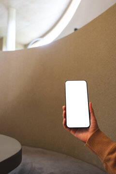 Vertical mockup image of a woman holding mobile phone with blank desktop screen in cafe