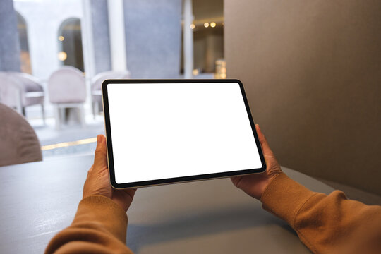 Mockup image of a woman holding digital tablet with blank white desktop screen in cafe