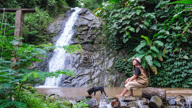 A woman sitting by the waterfall in the forest with a dog