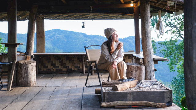A woman drinking coffee on wooden terrace and looking at nature views
