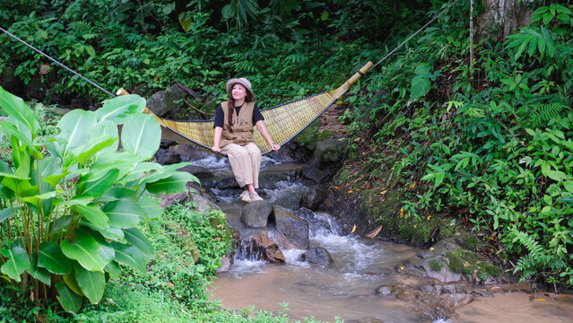 A woman sitting and relaxing in wooden hammock in the creek
