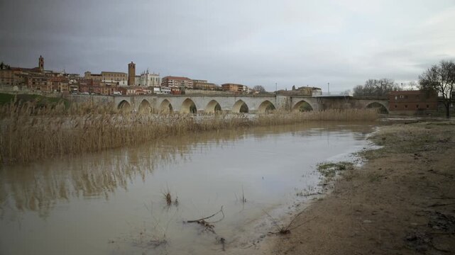 Man in Red Jacket Walking Along Flooded Muddy Riverbank in Winter