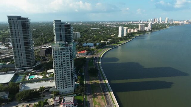 Cinematic drone view of Bayshore Boulevard's iconic curve in Tampa, Florida, with high-rise residences, palm-lined roads, and Hillsborough Bay stretching beyond.