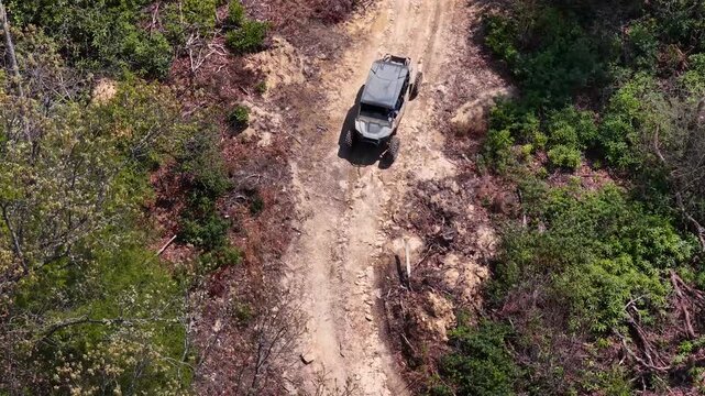 Overhead aerial drone video capturing a 4x4 off-roading ATV driving along a windy dirt path underneath the drone
