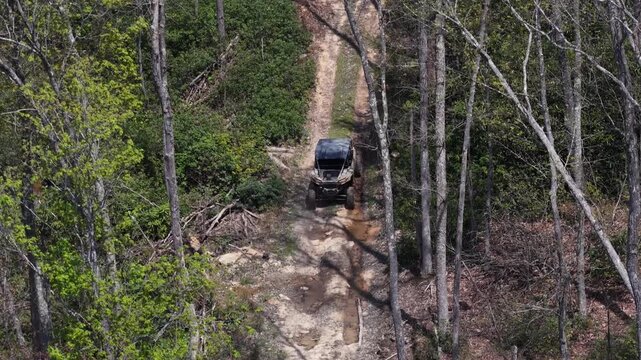 Drone aerial footage capturing a side-by-side driving through a forest trail, through a puddle between trees