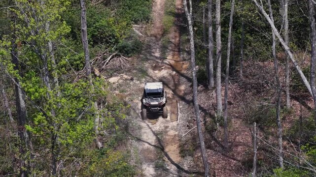 Overhead drone aerial footage capturing a dirty side-by-side driving through a mud puddle slowly on a spring day in West Virginia