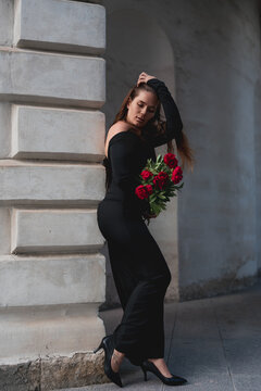 Peonies bouquet held by woman in black dress standing against classical stone archway with dramatic lighting