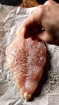 Raw Chicken Breast Being Prepared for Cooking with a Seasoning of Salt and Pepper on Top, Emphasizing the Freshness and Quality of the Meat.