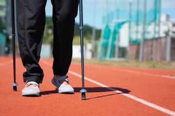 Obraz premium person walking with nordic walking poles on a red running track outdoor training lower body view with copy space for banner design concept of sport, rehabilitation, and fitness