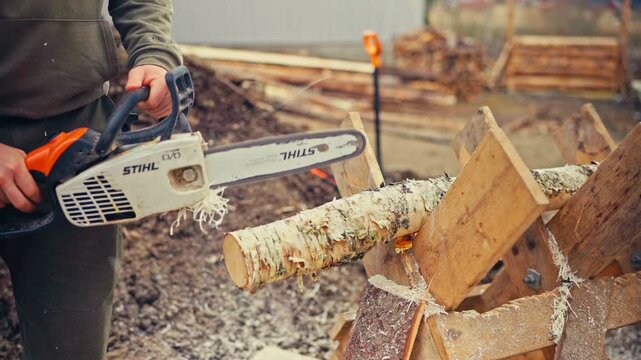 A man uses a chainsaw while working with lumber in a rural Norwegian setting