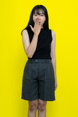 Shocked Young Woman In Casual Clothing Covering Her Mouth Against Vibrant Yellow Background