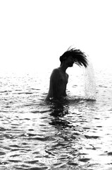 Fototapeta premium Silhouette of a young man flipping long hair back in sea water, port cranes background