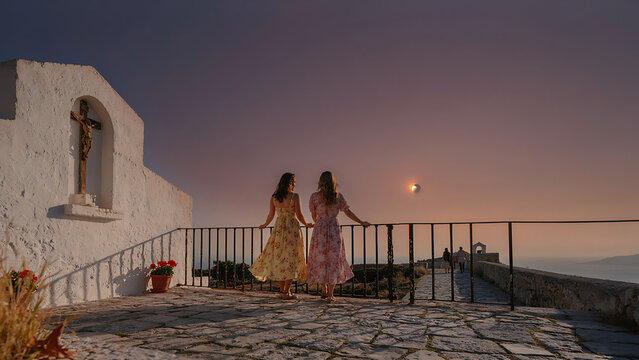 Two women stand on a chapel balcony gazing at a partial solar eclipse over the horizon during dusk, created with generative AI.