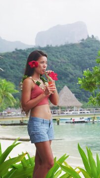 Vacation. Woman tourist drinking fruit drink cocktail at resort room balcony on beach. Vacation travel in Bora Bora, French Polynesia. Raw unedited vertical video of real woman model without makeup
