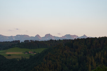 Fototapeta premium Scenic Gantrisch mountain panorama overlooking rolling countryside, forests and agricultural fields beneath a distant Swiss Alps skyline.