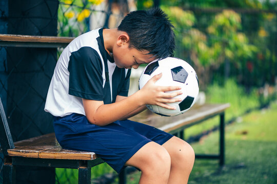 sad disappointed youth kid soccer player leaning his head over a football ball as a conceptual metaphor for sports psychology defeat loss pressure mental health fatigue and emotional failure