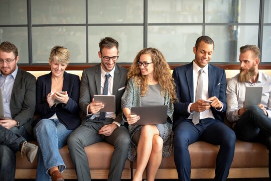 Diverse group of professionals sitting on a couch, using devices.