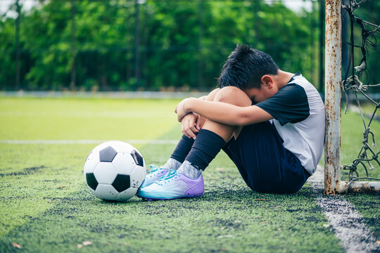 sad disappointed youth kid soccer player leaning his head over a football ball as a conceptual metaphor for sports psychology defeat loss pressure mental health fatigue and emotional failure