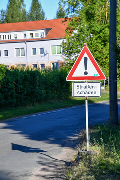 Verkehrsschild &bdquo;Stra&szlig;ensch&auml;den&ldquo; mit Gefahrzeichen an einer Wohnstra&szlig;e. Warnung vor besch&auml;digter Fahrbahn, Schlagl&ouml;chern, Stra&szlig;enreparatur, Verkehrssicherheit und kommunaler Infrastruktur.