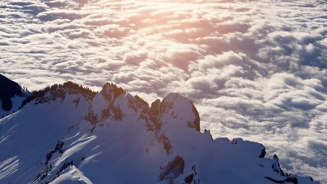 Aerial time lapse of majestic snow capped mountain peaks rising above a rolling sea of clouds illuminated by glowing sunset light