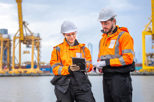 Port engineers team using tablet checking work at container terminal, professional industrial workers team in safety gear collaborating outdoors at shipping cargo port