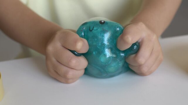 Sparkling teal squishy dumpling toy sits alone on white table showing cute printed face on white table. Glitter texture and curved smile make charming collectible dim sum themed character 