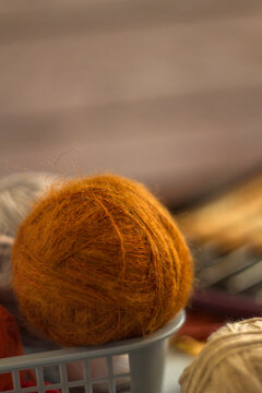 Cozy ball of fuzzy orange mohair wool yarn sitting in a basket. Close-up photo of soft knitting material for autumn handicraft, textile hobbies, and warm needlework concepts.