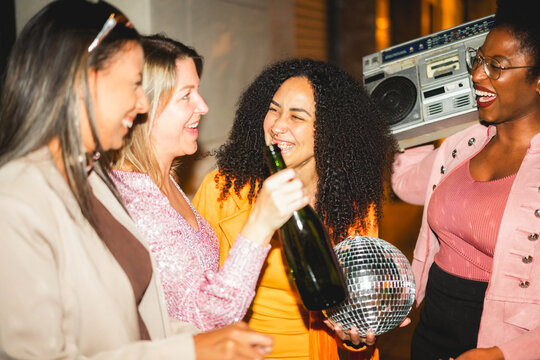 Group of multiracial girls having fun together drinking champagne and listening music outdoor - Party, nightlife and people lifestyle concept - Main focus on center latin girl face