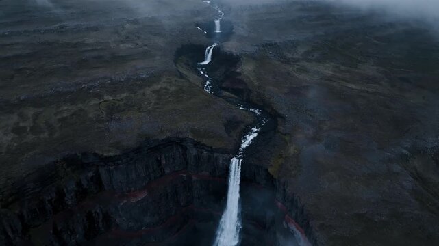 Aerial view of majestic hengifoss waterfall flowing down red layered basalt cliffs in icelandic highlands.