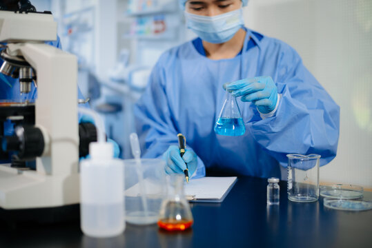 Two dedicated medical scientists in surgical protective gowns using a micropipette and microscope in research laboratory.
