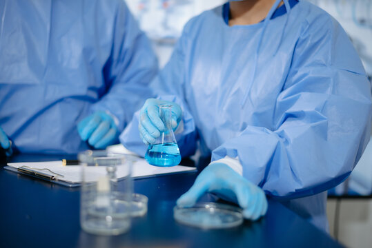 Two dedicated medical scientists in surgical protective gowns using a micropipette and microscope in research laboratory.