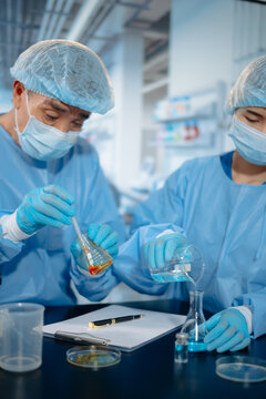 Two scientists collaborating in a modern biotechnology laboratory using laptop and microscope for biomedical research, healthcare innovation