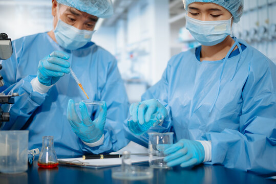 Two scientists collaborating in a modern biotechnology laboratory using laptop and microscope for biomedical research, healthcare innovation