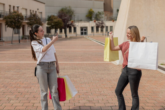 A happy young woman proudly shows her shopping bags while posing outdoors. Captures youth culture, friendship, fun and personal style. Horizontal image with copy-space.
