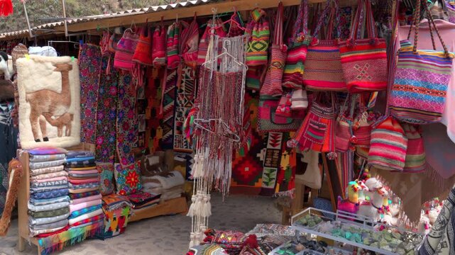 Wide angle view of colorful traditional Peruvian bags, alpaca fur rugs, and textiles displayed at a souvenir market in Peru.