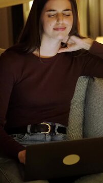Young freelancer feeling neck pain and muscle tension from prolonged computer use while working late at night, stretching to relieve the ache from a bad posture sitting on the couch