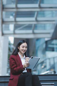 Focused woman in blazer types on laptop outdoors. Urban professional works remotely on stairs. She uses modern tech for business and connection.